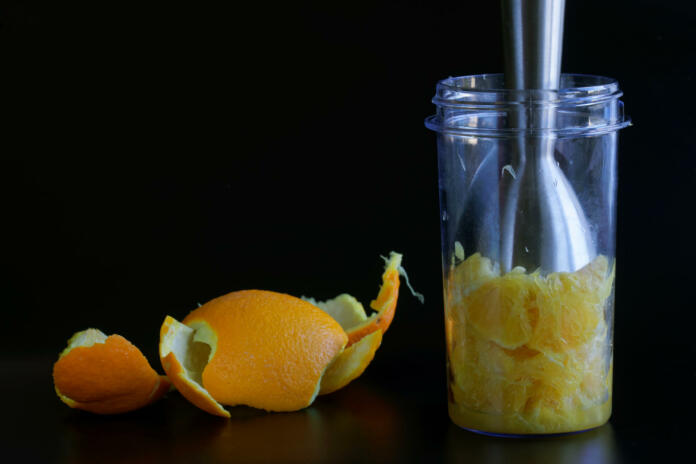 Fresh orange or grapefruit pulp in a blue transparent glass of a blender or shaker. The initial step in making a juice, cocktail or citrus smoothie. Black background. Close-up