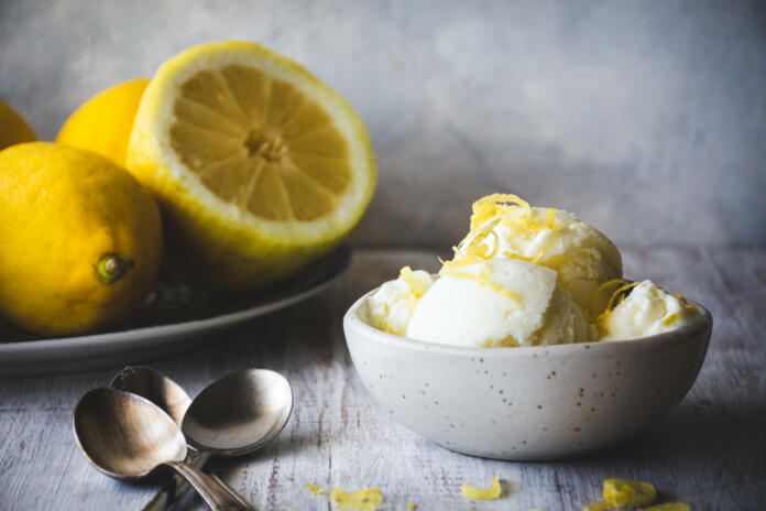 lemon ice cream in a bowl and a plate with lemons behind