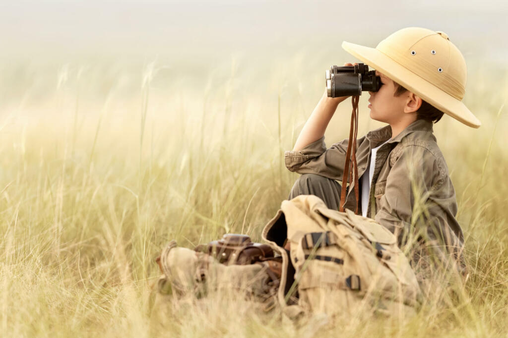 Little boy tourist looking into the distance with binoculars through the thick grass