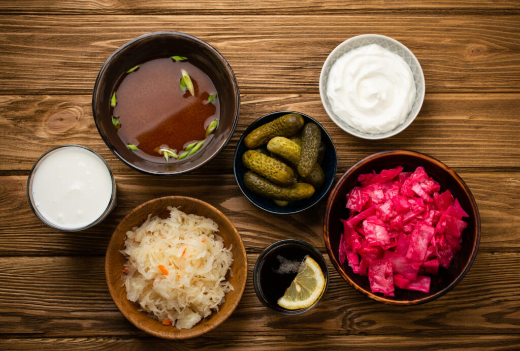 Top view of assorted fermented foods and drinks, sources of probiotics great for healthy gut and digestive system: kimchi, pickles, sauerkraut, miso soup, kombucha, yogurt, kefir, wooden background