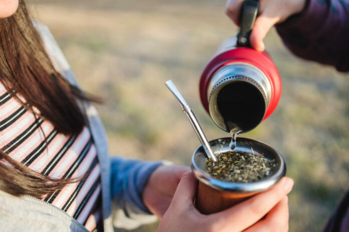 Two female friends brewing and drinking yerba mate, with a red thermos, in the countryside at sunset. Argentinian traditions and culture.