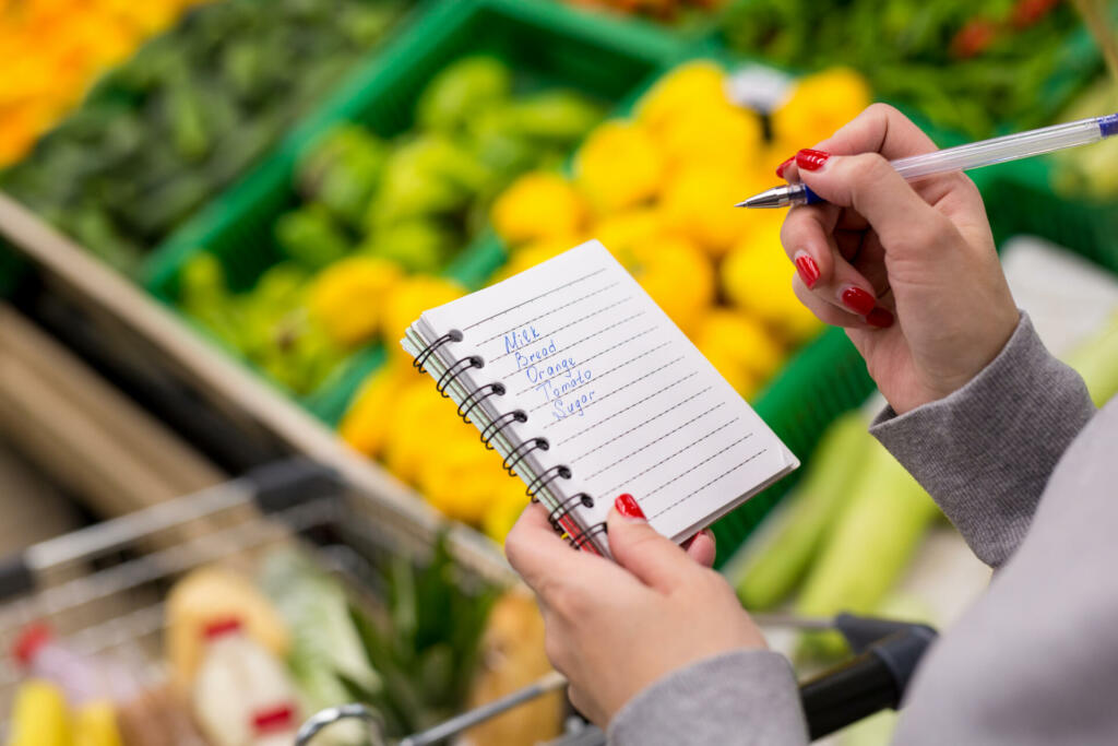 Woman with notebook in grocery store, closeup. Shopping list on paper