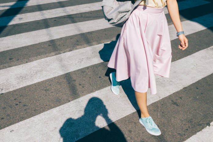 Young woman in a pink skirt and sneakers crossing the road in the summer