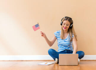 Objavljen natečaj za raziskovalno gostovanje v ZDA Young woman with USA flag using a laptop computer against a big interior wall
