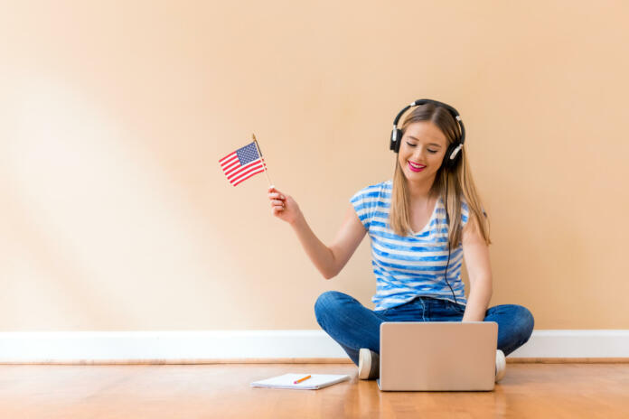 Young woman with USA flag using a laptop computer against a big interior wall