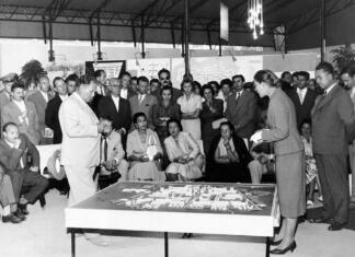 Zakaj je vaza podobna hiši? Od sistemskega do fantazijskega z oblikovalko Janjo Lap Janja Lap l. 1958 na velesejmu v Zagrebu jugoslovanskemu vrhu predstavlja projekt soseske za 5000 prebivalcev. Ob maketi stojita Josip Broz - Tito in Janja Lap, od leve proti desni sedijo zagrebški župan Većeslav Holjevac, Aleksandar Ranković, Jovanka Broz, Pepca Kardelj, Lidija Šentjurc, Vladimir Bakarić. Hrani MAO.