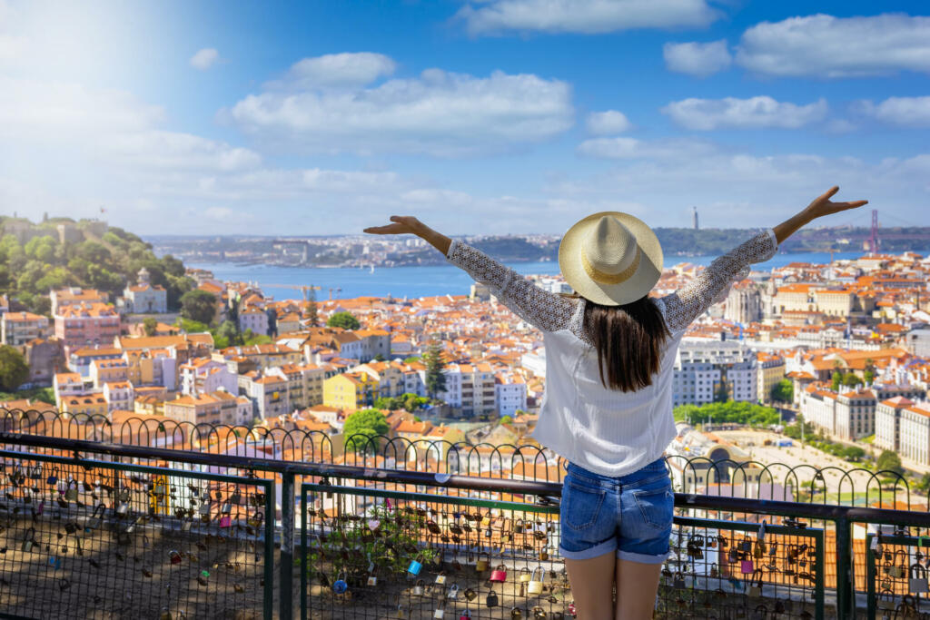 A happy tourist woman overlooks the colorful old town Alfama of Lisbon city, Portugal, and castle Sao Jorge on her sightseeing trip