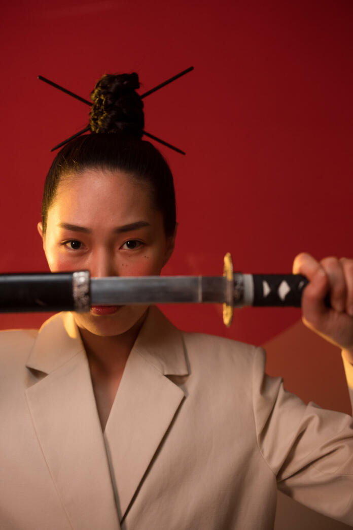 A woman holding a samurai while looking at the camera