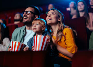 5 prednosti gledanja filmov A young joyful couple is with their daughter in the cinema, watching an exciting movie.
