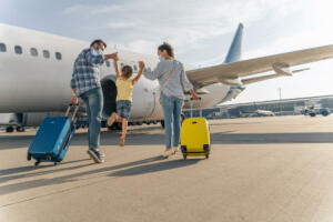 Back view of parents holding the hands of the child and going with suitcases to board the plane