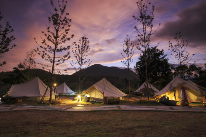 Canvas glamping bell tents in a green field with walkway at mountain view in beautiful sky with cloud before sunrise.