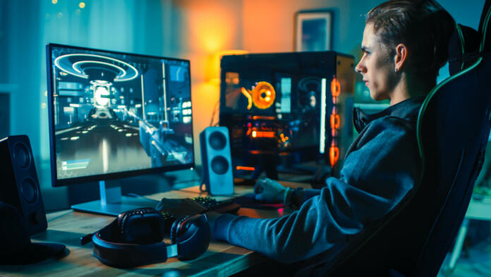 Cheerful Gamer Playing First-Person Shooter Online Video Game on His Powerful Personal Computer. Room and PC have Colorful Neon Led Lights. Cozy Evening at Home.