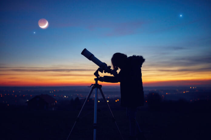 Child girl observing stars, planets, Moon and night sky with astronomical telescope.