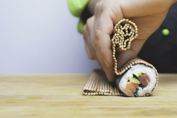 closeup of chef hands rolling up sushi on a bamboo mat