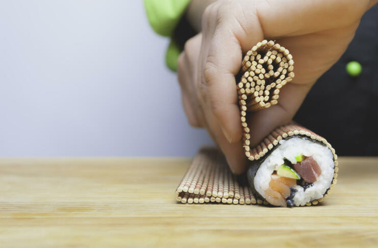 closeup of chef hands rolling up sushi on a bamboo mat