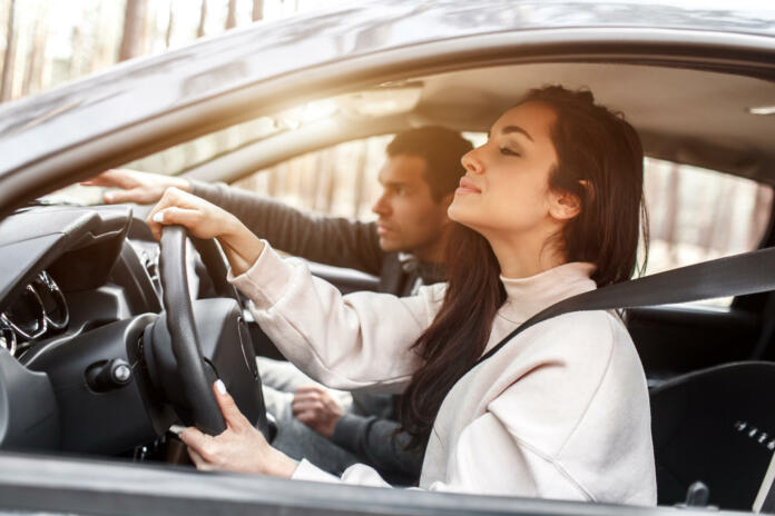 Driving instruction. A young woman learns to drive a car for the first time. Her instructor or boyfriend helps her and teaches her.