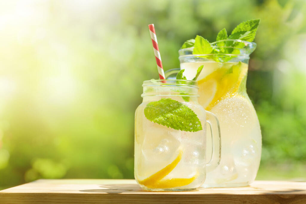 Fresh homemade lemonade with lemon and mint. Outdoor garden table on sunny day. With copy space