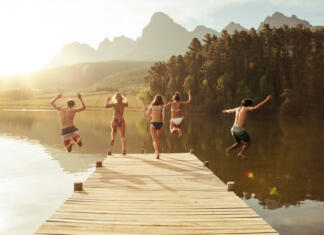 Najboljše lokacije za kopanje v naravi v Sloveniji Group of young people jumping into the water from a jetty. Group of friends jumping from pier in the lake on a sunny day.