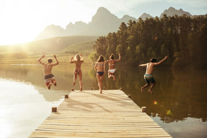 Group of young people jumping into the water from a jetty. Group of friends jumping from pier in the lake on a sunny day.