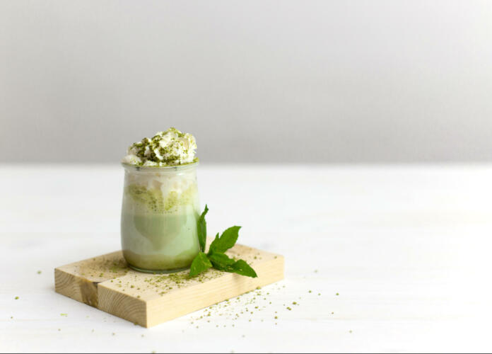 Healthy matcha dessert with aquafaba and mint. Glass jar on wooden board on neutral background with copy space. Green matcha for vegetarians. Weight loss concept, gluten free, sugar free dessert