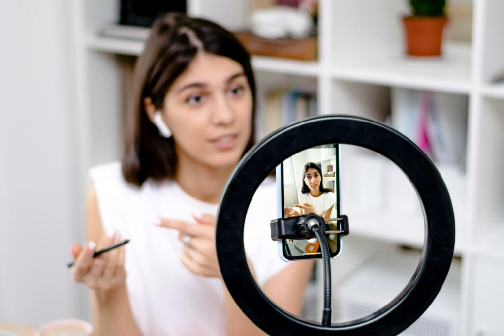 Influencer girl blogger talking smartphone,live recording video blog on social network at home.Social media live streaming concept.Focus on the phone, the girl in the background in a blur.