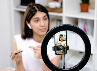 Kaj lahko Zakon o medijih pomeni za vplivneže? Influencer girl blogger talking smartphone,live recording video blog on social network at home.Social media live streaming concept.Focus on the phone, the girl in the background in a blur.