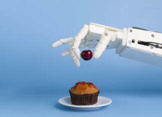 Ustvarjen robotski kuhar, ki se uči iz posnetkov Kitchen robotization. Robot hand putting fresh cherry on top of the cupcake, blue background