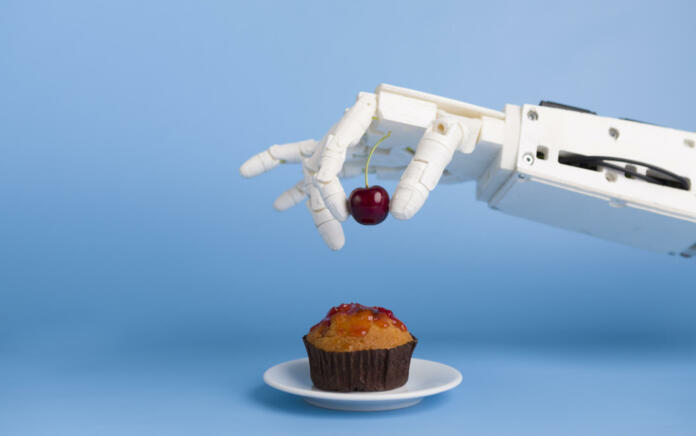 Kitchen robotization. Robot hand putting fresh cherry on top of the cupcake, blue background