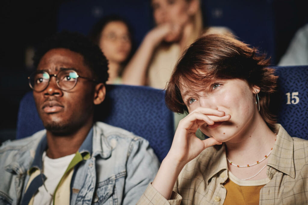Medium close-up portrait of young Black mana and Caucasian woman spending evening together crying while watching tragedy movie at cinema
