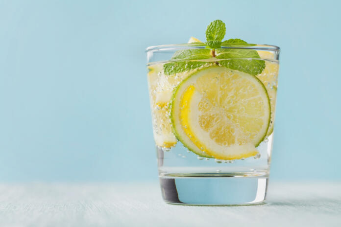 Mineral infused water with limes, lemons, ice and mint leaves on blue background, homemade detox soda water recipe