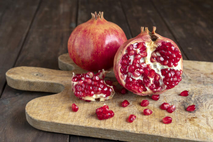Pomegranates on the cutting board on the old wooden kitchen table. Vegan and vegetarian food. Healthy eating. Ecological agriculture concept.