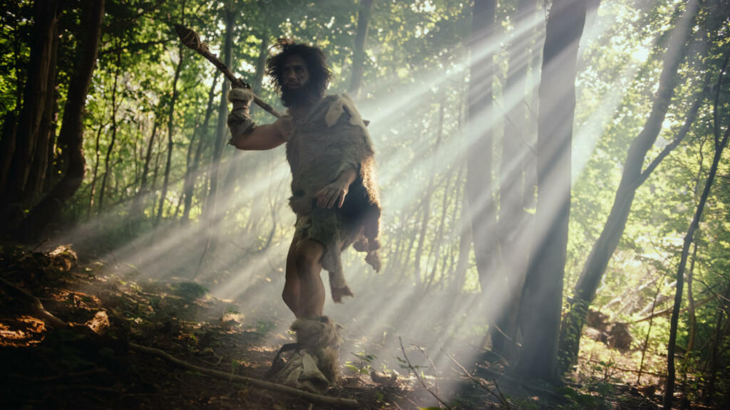 Portrait of Primeval Caveman Wearing Animal Skin and Fur Hunting with a Stone Tipped Spear in the Prehistoric Forest. Primitive Neanderthal Hunter Ready to Throw Spear in the Jungle