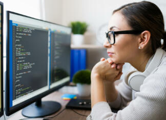 Vodič po nakupu monitorjev: vse, kar moraš vedeti v 2023 Profile of a hispanic freelancer wearing glasses and reading the coding software on the computer. Focused programmer checking the app code