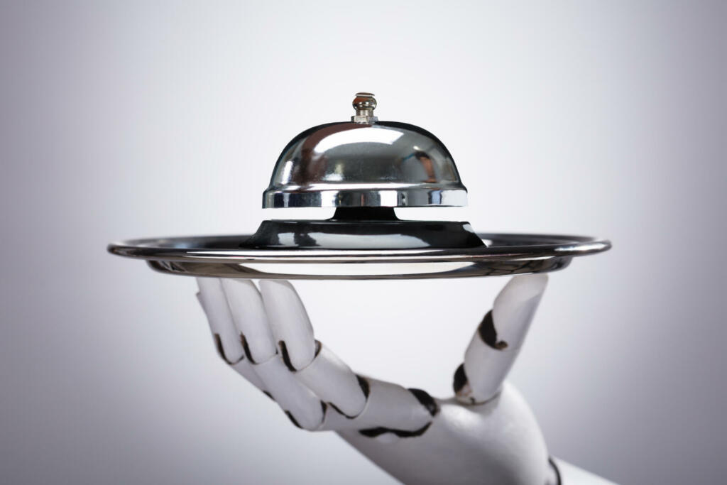 Robotic Hand Holding Service Bell In Plate Against Grey Background