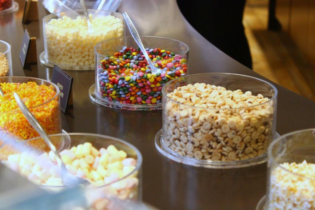 Shop with plastic bowls or containers full of white chocolate chips, multi colored sweets and toppings to add to the ice cream.