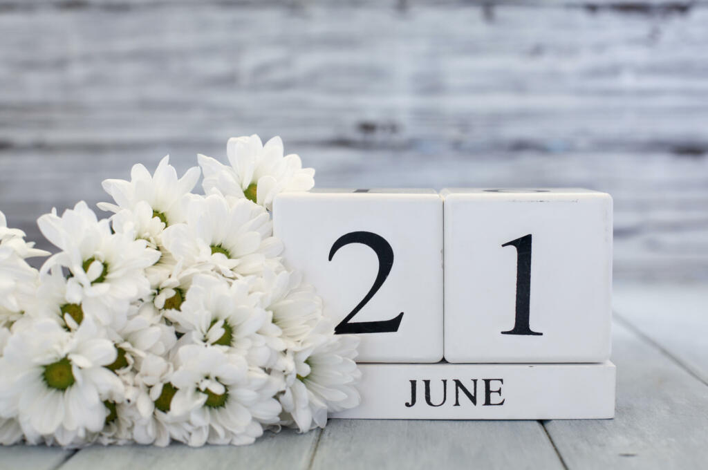 Summer Solstice White wood calendar blocks with the date June 21st and white daisies. Selective focus with blurred background.