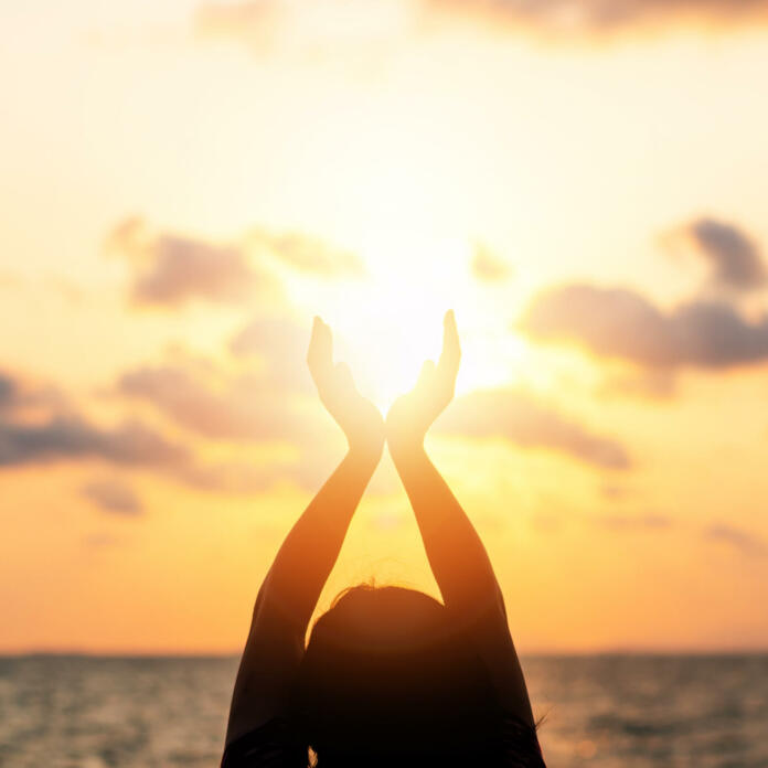 Summer sun solstice concept and silhouette of happy young womanâs hands relaxing, meditating and holding sunset against warm golden hour sky on the beach with ocean or sea background