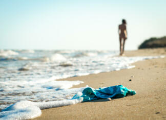 Nudistične plaže v naši bližini (FKK v Sloveniji in širše) swimsuit in the sand on the beach near the sea surf on the background of a naked female figure and blue sky