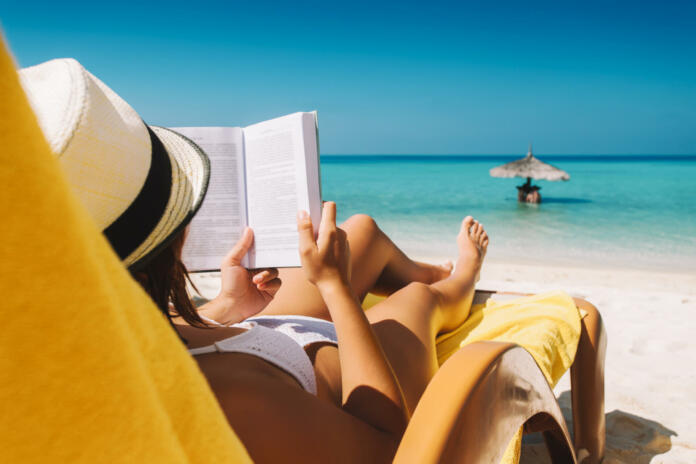 Woman on sunbed reading book under parasol at tropical island