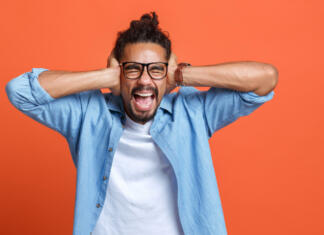 Kaj je tinitus? Ko piskanje v ušesih postane težava Young emotional african american man with hands on ears gesturing don't want to hear and screaming while standing isolated over orange studio background, annoyed mixed-race guy ignoring loud noise