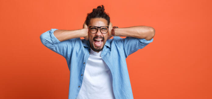 Young emotional african american man with hands on ears gesturing don't want to hear and screaming while standing isolated over orange studio background, annoyed mixed-race guy ignoring loud noise