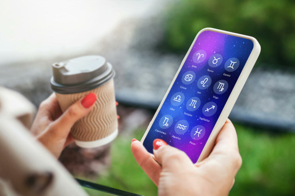 a woman holds a mobile phone with an astrological application and looks at the forecast for the future for the signs of the zodiac holding a cup of coffee in her hands