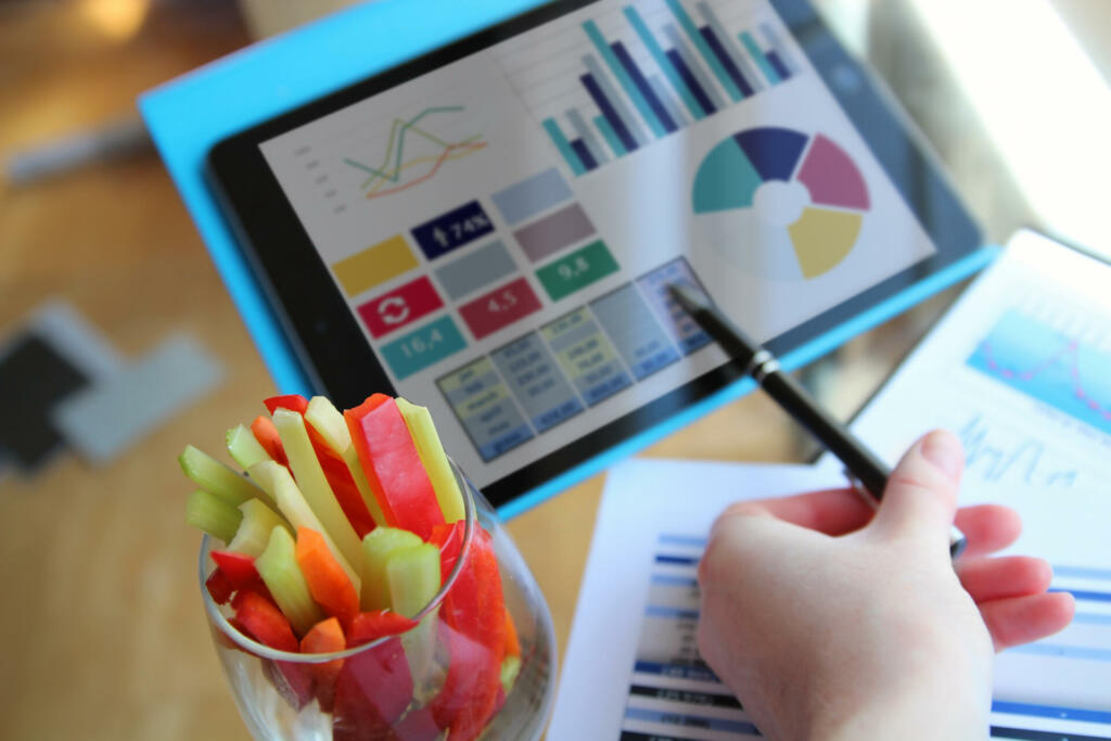 Businessman  working and analyzing financial figures on a graphs on a tablet. Lunch time with healty snack, vegetables.