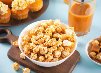Kokice s karamelo: Kako pripraviti najboljšo karamelno pokovko? Caramel popcorn snack on white bowl with delicious cupcakes and caramel syrup in jar on the background.