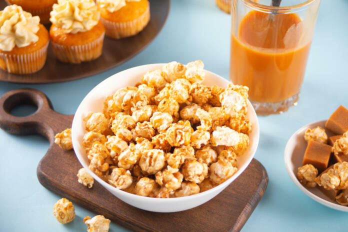 Caramel popcorn snack on white bowl with delicious cupcakes and caramel syrup in jar on the background.