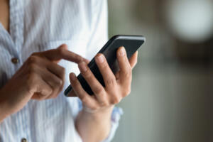 Close up cropped of woman holding smartphone in hand, typing on screen writing message in social network, young female chatting or shopping online, browsing mobile device apps, ordering in internet