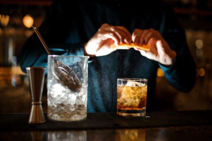 curly guy the barman in a blue shirt finishes preparing an alcoholic cocktail Old Fashioned with ice adding an orange bitter