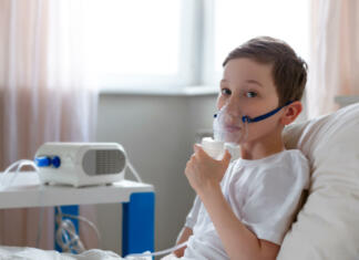 Kaj je cistična fibroza? Simptomi, nastanek, zdravljenje in vse ostalo Cute boy inhalation therapy by the mask of inhaler. Kid with respiratory problem or asthma with copy space. View of portable nebulizer with smoke from oxygen mask.