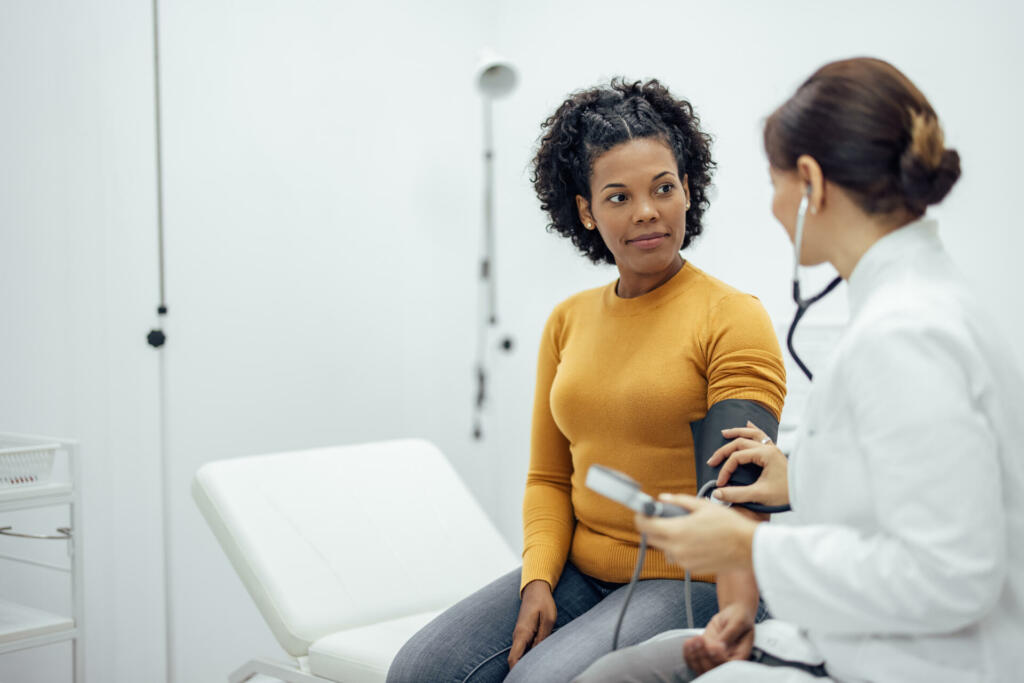 Doctor measuring blood pressure to a smiling woman as a part of a medical exam.