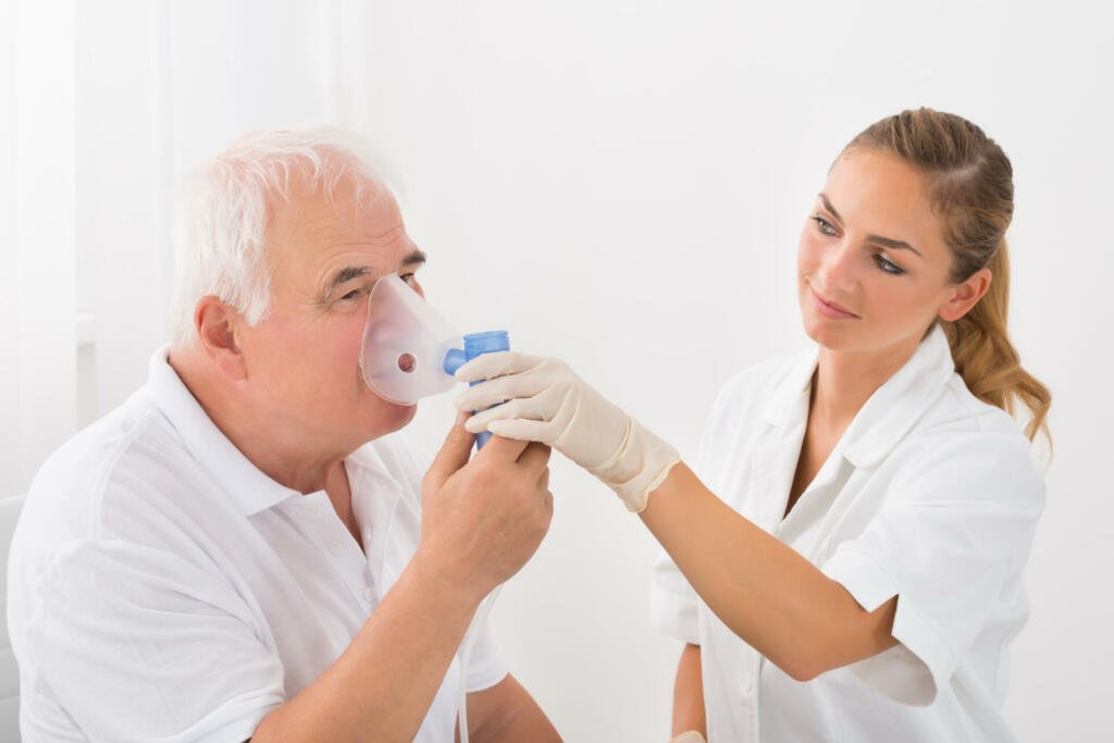 Female Doctor Looking At Senior Male Patient Inhaling Through Oxygen Mask